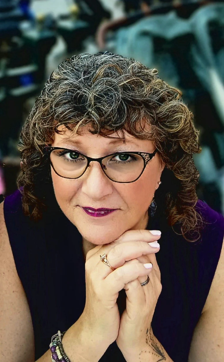 Vonnie Rambo-Henry with curly auburn hair and cat-eye glasses, her chin resting on her folded hands.